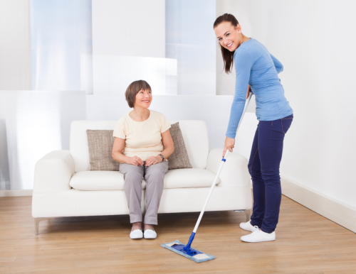 caregiver cleaning the floor with a mop while a senior woman sitting on the sofa